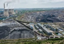 China Mulling Extraction of Critical Metals from Coal Waste Aerial view of a large industrial complex with cooling towers emitting steam, coal stockpiles, and processing buildings beside rail lines and conveyors.
