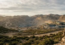 Geopolitical Impacts Controlling Global Copper Mining Supply Open-pit quarry in a desert landscape with conveyor belts and heavy machinery at work beneath a cloudy sky