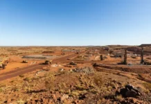 Fenix Advances Iron Ore Mine Development at Weld Range Arid construction site with heavy machinery and drill rigs spread across red dirt landscape under a clear blue sky.