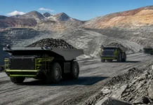 SANY Ships Autonomous Electric Mining Trucks to South America Open-pit mine with large dump trucks hauling ore along a dusty road, terraced earth walls in the background.