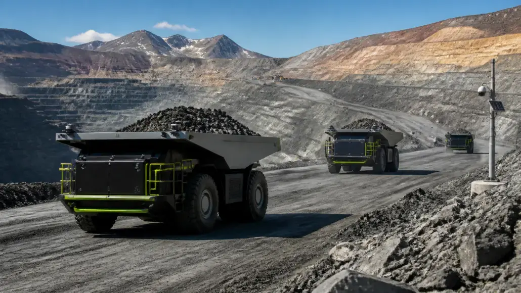 Open-pit mine with large dump trucks hauling ore along a dusty road, terraced earth walls in the background.