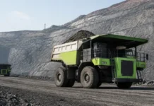 Zijin Longking Launches 230-Tonne Battery Mining Truck Large green mining dump truck at a rock quarry, on a dusty road with steep rock walls behind it.
