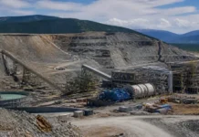 Blackwater Gold Mine Expansion Drives Production Growth Open-pit mining site with conveyor belts, large machinery, and storage tanks against terraced rock faces and distant hills.