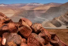 Codelco Profit Surges as Copper Prices Offset 11% Production Decline Close-up of reddish brown rocks in the foreground with a desert canyon and winding road in the distance.