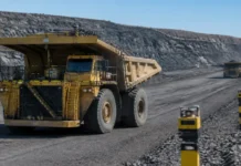 Komatsu Advances Collision Prevention Technology With TRL4 Certification Large yellow mining dump truck driving on a gravel road at an open-pit mine with terraced rock walls nearby