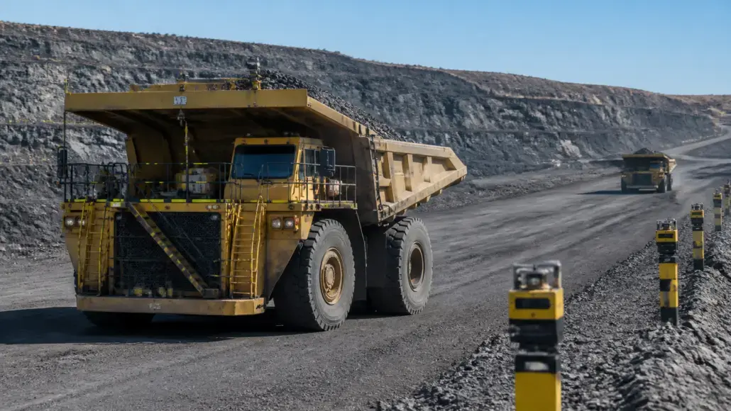 Large yellow mining dump truck driving on a gravel road at an open-pit mine with terraced rock walls nearby