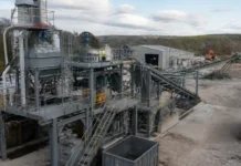 UK Opens Applications for ยฃ25 Million Critical Minerals Fund to Accelerate Domestic Projects Industrial processing plant with metal framework, stairs, and conveyors; workers stand on platforms inspecting equipment outdoors.