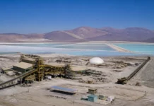 Argentina and South Korea Forge Critical Minerals Partnership on Lithium Value Chain Aerial view of a mining facility with yellow scaffolding and conveyor belts beside turquoise salt ponds and distant purple mountains under a clear blue sky.