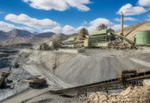 Boliden’s Nexa Resources Acquisition Expands Its Base-Metals Portfolio Open-pit mining site with terraced slopes, heavy trucks, and a green processing plant connected by conveyors under a blue sky.