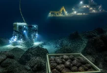 US Advances Seabed Mining in International Waters Underwater scene: a blue-lit ROV on the seabed near a crate of rocky nodules, with a illuminated support ship and crane in the background above.