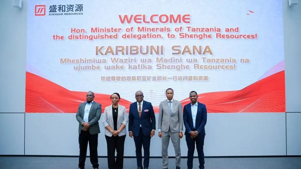 Group of five professionals in business attire posing in front of a large welcome banner at a corporate event.