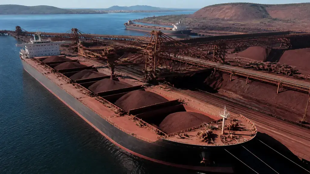 A bulk carrier at a coal terminal with large brown coal piles and conveyor belts nearby.