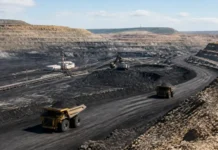 Navajo Coal Mine Expansion Wins Federal Approval Open-pit coal mine with large haul trucks driving on a dirt road and conveyor belts in the excavation pit.